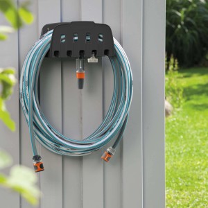 Porta tubo da parete Gardena con tubo da giardino arrotolato e accessori per l'irrigazione.