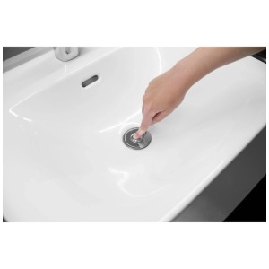 Mano preme tappo lavandino universale Drain Magic cromato con filtro in un lavabo bianco.