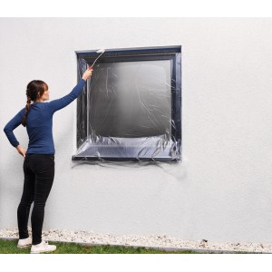 Femme recouvrant une fenêtre avec le film de masquage Tesa Easy Cover Outdoor. Protection contre la peinture lors de travaux extérieurs.