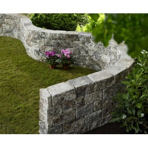 Geschwungene Mauer aus Vigneto Jura-Nuanciert Mauersteinen im Garten mit Blumen.