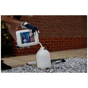 Person gießt Easihold Mulch & Steinbinder aus weißem Kanister in Sprühflasche auf Kiesfläche. Anwendung Gartendekoration.