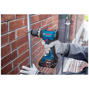 Trapano avvitatore a percussione a batteria Bosch Professional GSB 18V-65 in uso su una parete di mattoni.