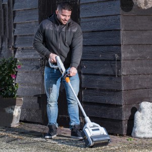 Uomo che utilizza la spazzola a rullo Batavia Maxxbrush per pulire le pavimentazioni in giardino.