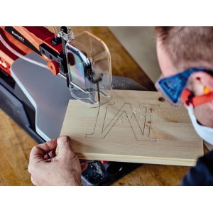 Einhell Dekupiersäge mit Holzstück, in das ein "M" gesägt wird. Zubehör: Sägeblatt-Set.