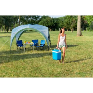 Frau trägt blaue Campingaz Icetime Plus 30 l Kühlbox auf einer Wiese.