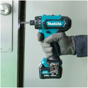 Visseuse sans fil Makita vissant dans une porte, batterie et lumière LED visibles.