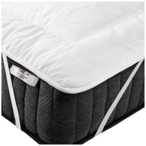 Surmatelas blanc Yangra 160x200 cm sur un matelas foncé avec des élastiques.