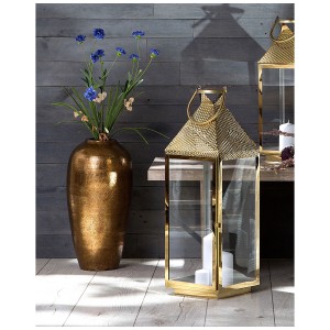 Vaso decorativo Lorca in terracotta marrone dorato di Beliani con fiori, accanto a una lanterna dorata.