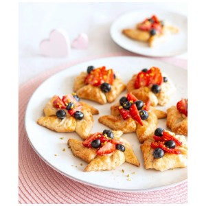 Goldbraunes Gebäck mit frischen Erdbeeren, Heidelbeeren und Pistazien auf weißem Teller, gebacken in Backform.