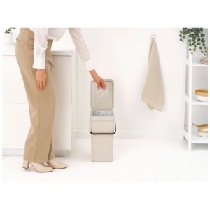 Brabantia Pattumiera Sort & Go, 16 l, Soft Beige. Donna che getta rifiuti nel cestino aperto.