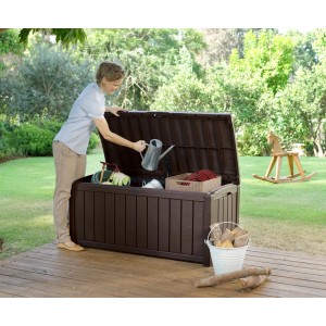 Coffre de rangement Keter Glendwood marron ouvert avec outils de jardin et femme mettant un arrosoir à l'intérieur.