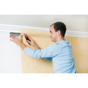 Mann schneidet Tapete mit LUX Kombi-Set (Lineal, Profil, Cutter) für Tapezierarbeiten.