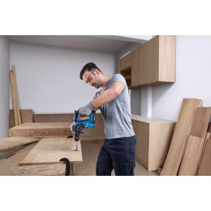 Un homme perce un trou dans une planche de bois avec un perforateur sans fil Bosch Professional GBH 18V-18 X.