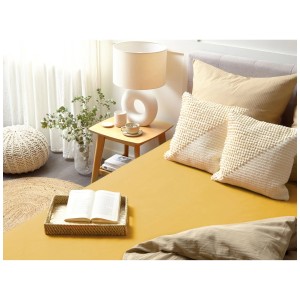 Lenzuolo con angoli in cotone giallo senape 90x200 cm su un letto con cuscini e comodino.