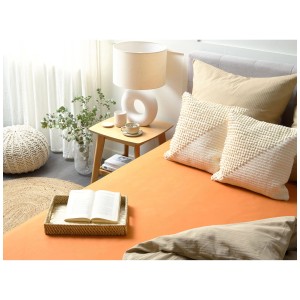 Lenzuolo con angoli arancione Janbu in cotone 200x200 cm su letto king-size con cuscini.