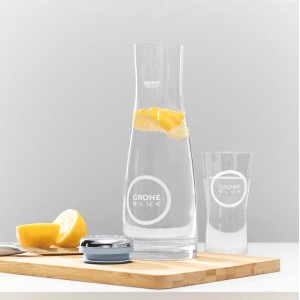 Caraffa in vetro Grohe Blue con acqua, limone e bicchiere su tagliere di legno.