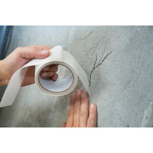 Application du ruban de pontage de fissures LUX (10 m x 50 mm) sur un mur fissuré.
