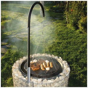 Barbecue et foyer en gabion avec grille et bras pivotant dans le jardin.