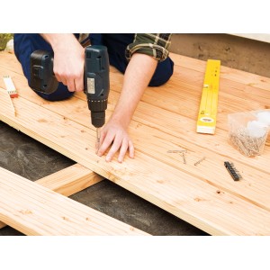 Construction de terrasse : un homme visse une vis à terrasse à tête fraisée lentille avec entraînement TX dans une planche de bois.