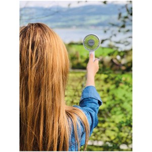 Femme tenant un ventilateur à main vert Lacerta devant un paysage. Ventilateur portable pour les déplacements.
