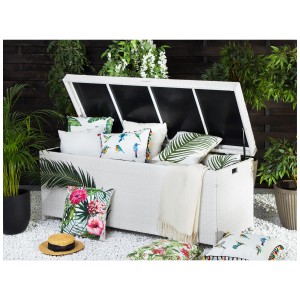Coffre de rangement Modena en rotin blanc ouvert avec coussins et couvertures dans le jardin.