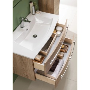 Vasque en céramique Oscar, courbée, blanche, avec tiroirs ouverts et accessoires de salle de bain.