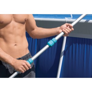 Homme tenant la perche télescopique du kit de nettoyage Intex Deluxe pour piscines devant une piscine bleue.