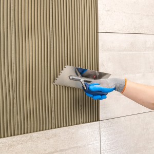 Applicazione di Knauf Flexkleber Naturstein con spatola dentata su piastrelle.