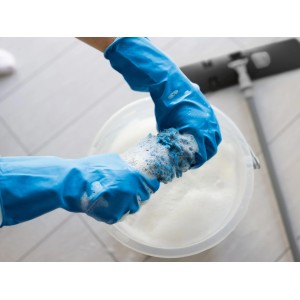 Mani con guanti riutilizzabili Robust taglia S blu che strizzano una spugna in un secchio d'acqua saponata.
