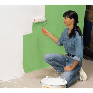 Femme peignant un mur au rouleau, papier de protection LUX recommandé pour la couverture.