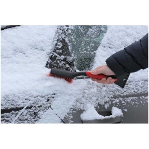 Balai à neige Nigrin avec grattoir à glace en cours d'utilisation pour enlever la neige d'une vitre de voiture.