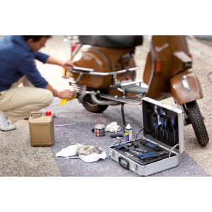 Homme nettoyant un scooter sur LUX Abdeckvlies. Boîte à outils et bidon d'huile à disposition.