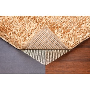 Sous-tapis OBI 80x130 cm sous un tapis sur sol en bois et en pierre.
