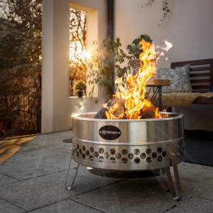 Brasero Petromax Tyropit en acier inoxydable avec feu, créant une ambiance de feu de camp dans le jardin.