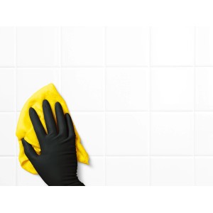 Mano con guanto monouso nero (taglia L) e panno giallo che pulisce piastrelle bianche.