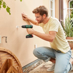 Uomo che fora un muro esterno con un trapano avvitatore a percussione Bosch 18V.
