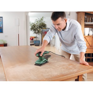 Homme ponçant une table avec la ponceuse vibrante Bosch PSS 200 A. Ponceuse avec système microfiltre en utilisation.