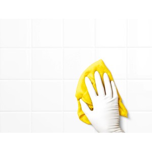 Mano con guanto monouso in lattice bianco pulisce piastrelle bianche con panno giallo.