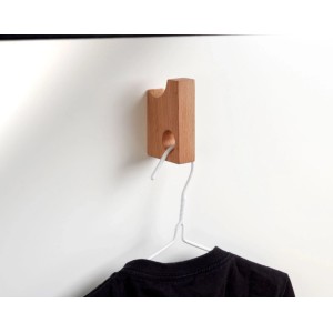 Hettich Wandhaken Typ 77 aus hellem Buchenholz an weißer Wand, mit Kleiderbügel und schwarzem T-Shirt.