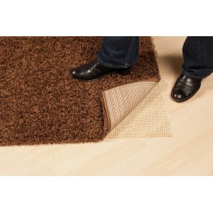 Tapis sur sous-tapis en jute (80x130 cm) sur plancher en bois, maintenu par des pieds.