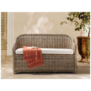 Panca da giardino Beliani Susua in rattan naturale intrecciato con cuscino bianco e coperta arancione.