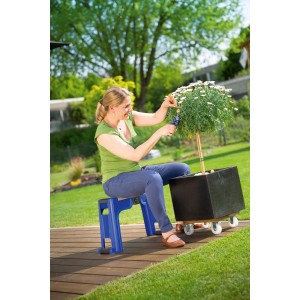 Femme assise sur tabouret de jardin LUX bleu avec coussin de genoux, taillant une plante dans le jardin.