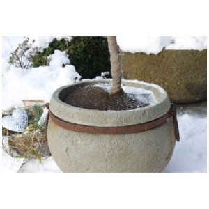 Fioriera effetto pietra con tronco avvolto in juta in un giardino invernale.