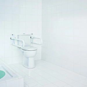 Barre d'appui WC blanche rabattable, standard, installée à côté d'une toilette dans une salle de bain carrelée de blanc.