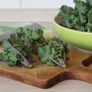 Chou de Bruxelles Flower Sprout bio sur planche en bois, feuilles vertes et tiges violettes.