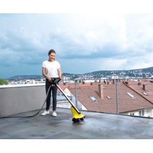 Femme nettoyant une terrasse avec le Kärcher PCL 4 et des brosses rouleaux pour surfaces en pierre.