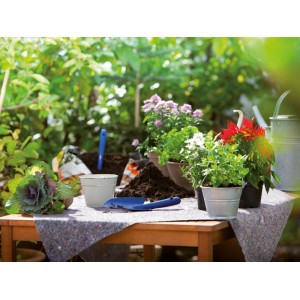 Feutre de protection comme base pour rempoter des plantes dans le jardin, avec de la terre, une pelle et un arrosoir.