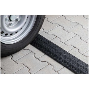 Cartrend Kabelbrücke aus Gummi, schwarz, 100 cm, mit einem Reifen auf Pflastersteinen.