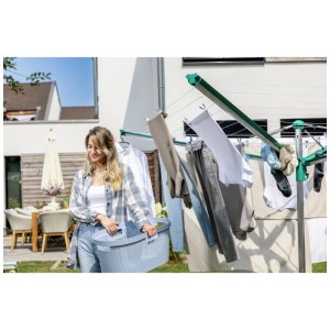 Femme avec séchoir rotatif Leifheit Linomatic 600 Deluxe et panier à linge dans le jardin.