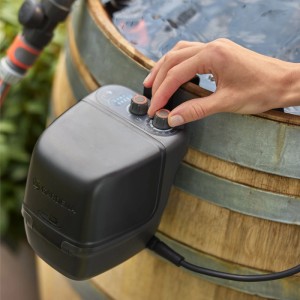 Pompe de récupération d'eau de pluie sans fil Gardena 2400 ComfortAutomatic Set sur cuve avec main sur la commande.